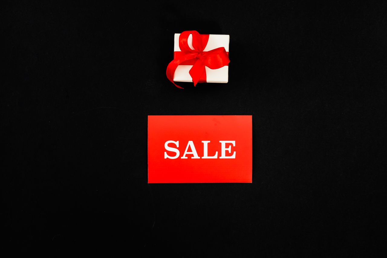 Top view of a red sale card and gift box with a ribbon on a black background. Perfect for shopping promotions.