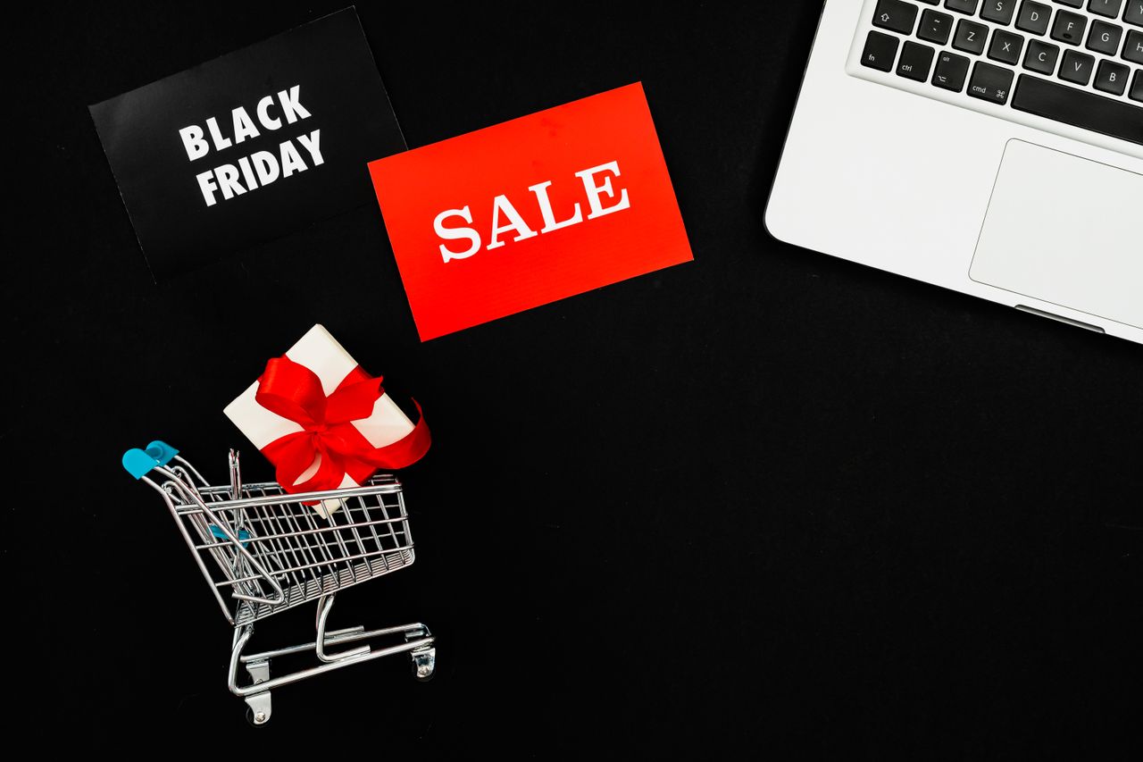 our-value Top view of Black Friday sale with red gift box and laptop on black background.