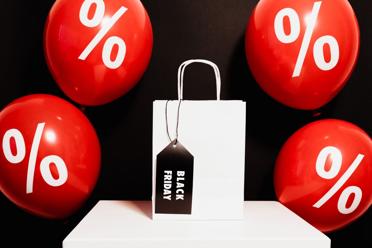 about-02 White shopping bag with Black Friday tag surrounded by red discount balloons.