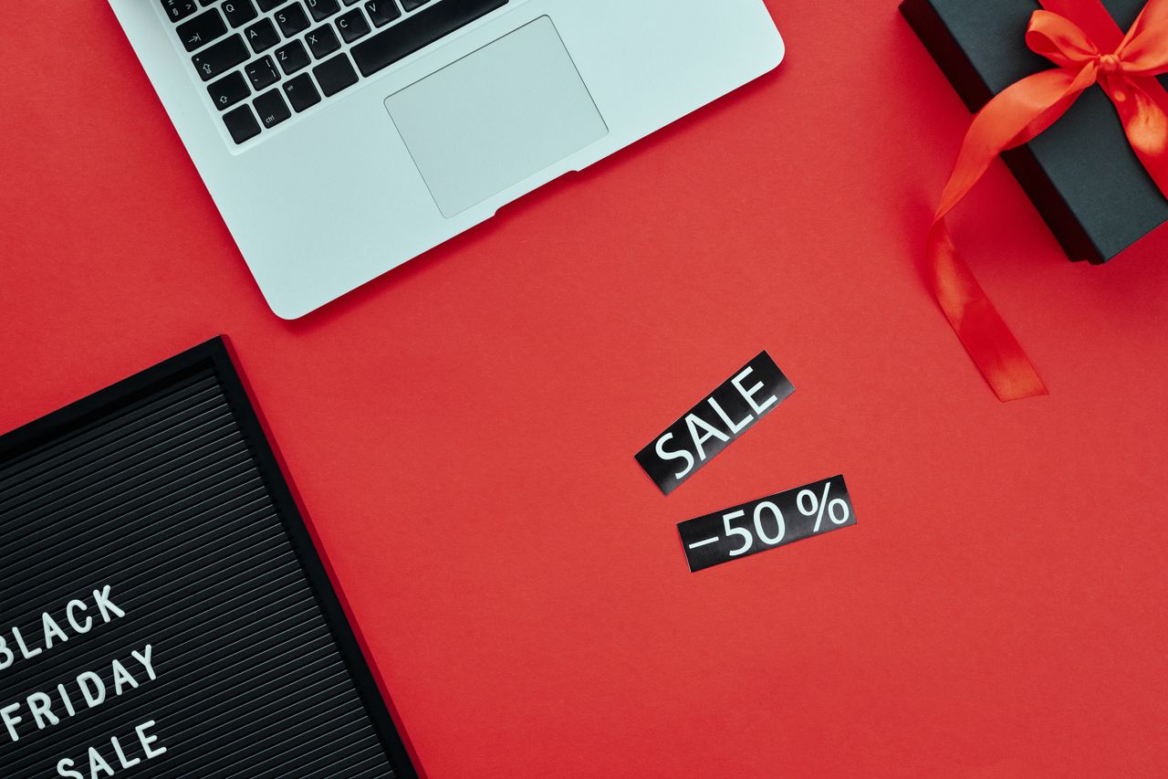 why-choose-us-02 Overhead view of a laptop and gift box on a red surface with Black Friday sale sign.